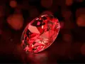 A brilliant, faceted ruby, the july birth color, glows with deep red fire against a dark, bokeh background.