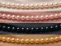 Rows of pearl color beads: cream, pink, black, and gold, draped on satin fabric.