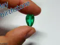 Fingers hold a pear-shaped emerald, the vibrant green gem representing the May birthstone.