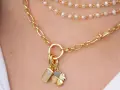 Layered necklaces featuring different types of gold chains, including a figaro chain and a pearl strand, adorned with charms.
