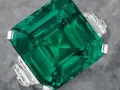 A stunning emerald ring, showcasing a large, square-cut green gemstone, possibly the most expensive gemstone, surrounded by smaller diamonds.