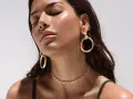 A woman with closed eyes showcases various types of dangling earrings, including large gold hoops and smaller ear cuffs.