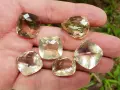 A hand holds six faceted lemon quartz gemstones, showcasing their pale yellow and brown hues. These stones are often associated with the lemon quartz meaning of clarity and optimism.