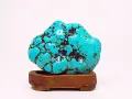 A vibrant turquoise stone, reminiscent of a Sagittarius stone, rests on a wooden stand. Its matrix pattern resembles a starry night sky.