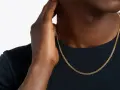 A man's hand touches his neck, showcasing a sleek gold chain length for men.