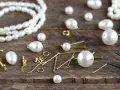 A collection of cultured pearls, meaning their natural beauty and value, are scattered with jewelry-making findings on a wooden surface, ready to be crafted into elegant pieces.