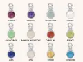 A collection of silver charms, each featuring a different colored gemstone representing birthstones for months: Garnet, Amethyst, Aquamarine, Crystal, Chrysoprase, Rainbow Moonstone, Carnelian, Peridot, Lapis, Opal, Citrine, and Turquoise.