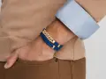 A man's wrist displays two stylish bracelet types: a blue braided leather bracelet with gold accents and a diamond-studded gold chain bracelet.