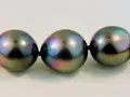 A close-up of a strand of dark, iridescent pearls with peacock green and purple overtones.