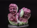 Two cherubic figures carved from ruby in zoisite, one resting its head on its hand, the other holding a green leaf-like element.