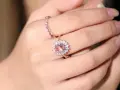 A hand wears two rings. The main ring features a large, peachy-pink morganite surrounded by small diamonds.