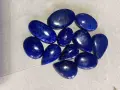 A collection of polished, deep blue Afghanistan gemstones, likely lapis lazuli, are scattered on a textured surface.