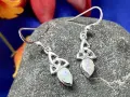Silver Celtic knot earrings with opals, reminiscent of ancient Celtic birthstones, rest on a textured stone.