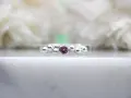 A silver ring with a central pink sapphire, the birthstone for September, surrounded by small silver spheres.