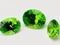 Three faceted peridots, the august 3rd birthstone, gleam with vibrant green light against a white background.