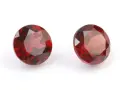 Two deep red, faceted gemstones, the traditional capricorn birthstone, are displayed on a white background.