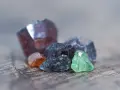 Raw gemstones in various colors, including deep red, orange, grey, and green. The deep red stone might be the birthstone for January.