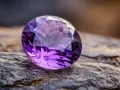 A faceted amethyst, the beautiful feb birthstone, rests on a textured rock.