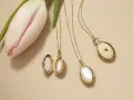 Gold lockets featuring mother of pearl, a lustrous material from shells, lie beside a delicate pink tulip.