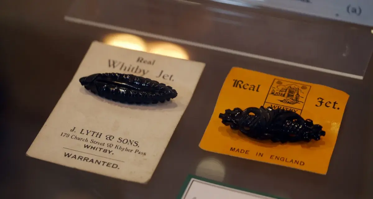 Two antique black jet stone brooches, one on a cream card from J. Lyth & Sons, Whitby, the other on a yellow card.