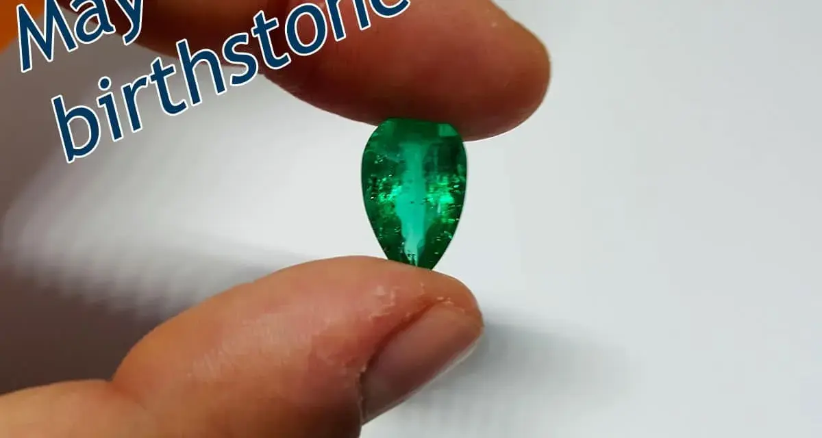 Fingers hold a pear-shaped emerald, the vibrant green gem representing the May birthstone.