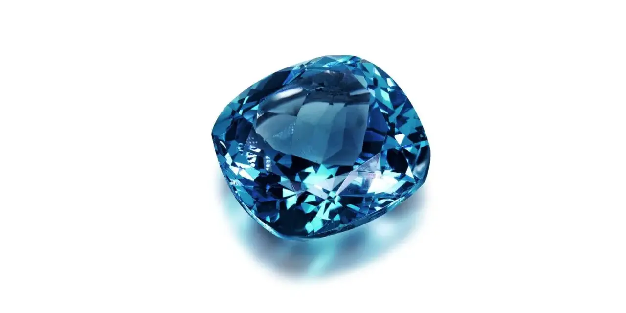 A cushion-cut blue gemstone, likely sapphire, what is September's birthstone, sparkles against a white background.