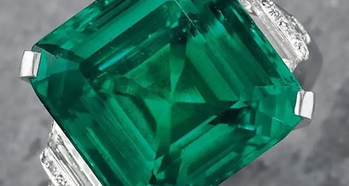 A stunning emerald ring, showcasing a large, square-cut green gemstone, possibly the most expensive gemstone, surrounded by smaller diamonds.