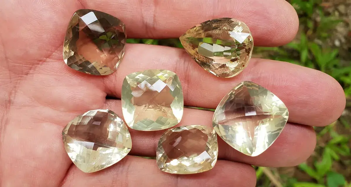 A hand holds six faceted lemon quartz gemstones, showcasing their pale yellow and brown hues. These stones are often associated with the lemon quartz meaning of clarity and optimism.