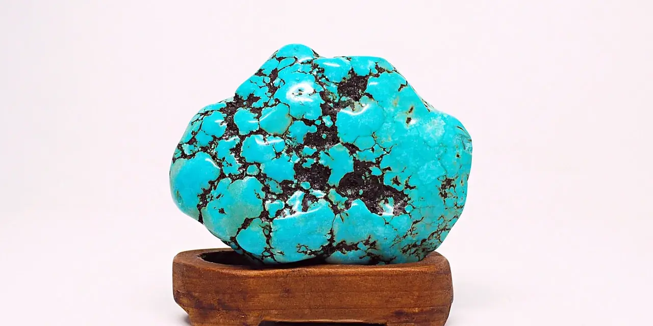 A vibrant turquoise stone, reminiscent of a Sagittarius stone, rests on a wooden stand. Its matrix pattern resembles a starry night sky.
