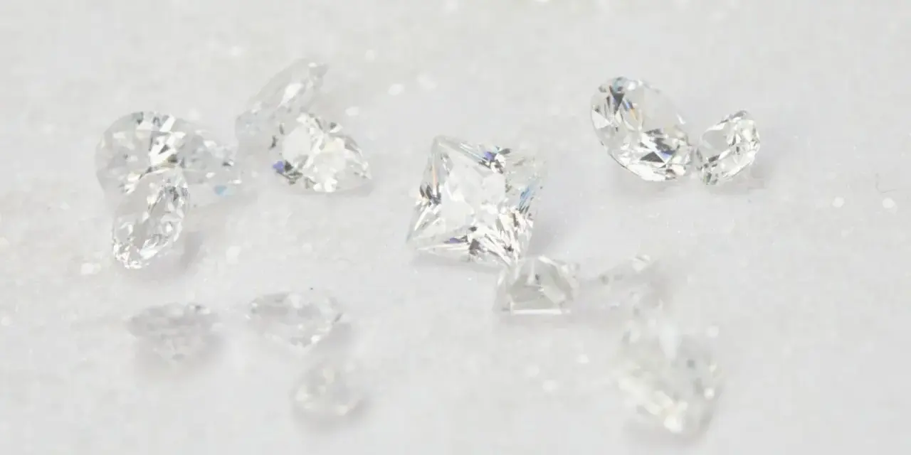 Scattered diamonds, some square-cut, others pear-shaped, on a white, glittery surface. These beautiful stones remind us of the dark reality of what is a blood diamond.