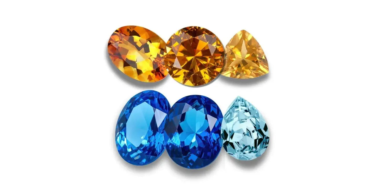 A collection of faceted gemstones, including warm orange and yellow topaz birthstones, and cool blue and aquamarine stones, arranged in two rows.