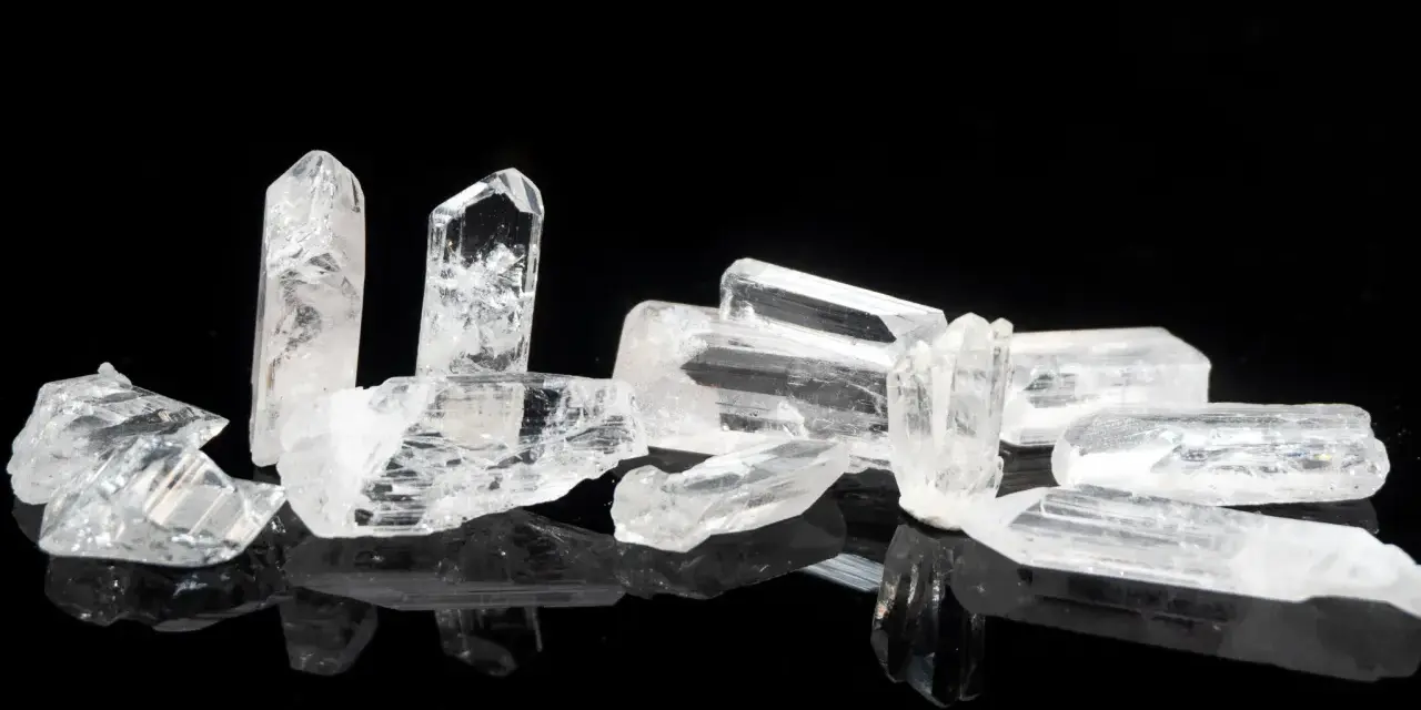 Raw danburite crystals on a black reflective surface, hinting at their powerful danburite metaphysical properties for spiritual growth and angelic connection.