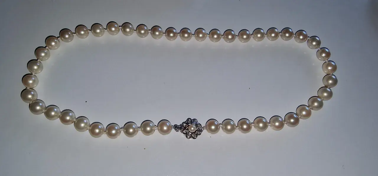 A pearl necklace with a diamond clasp. Learn how to tell if pearls are real by examining their luster and surface imperfections.