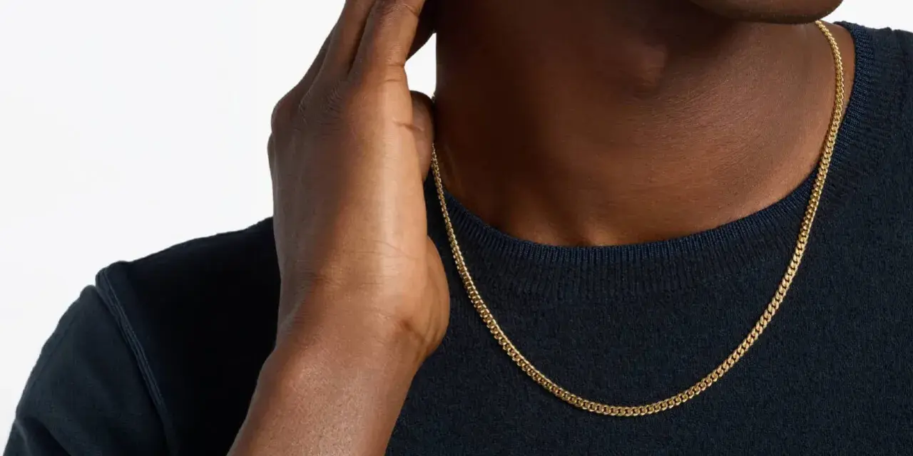 A man's hand touches his neck, showcasing a sleek gold chain length for men.