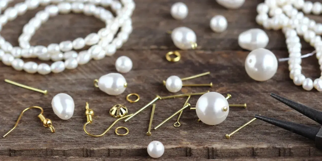 A collection of cultured pearls, meaning their natural beauty and value, are scattered with jewelry-making findings on a wooden surface, ready to be crafted into elegant pieces.