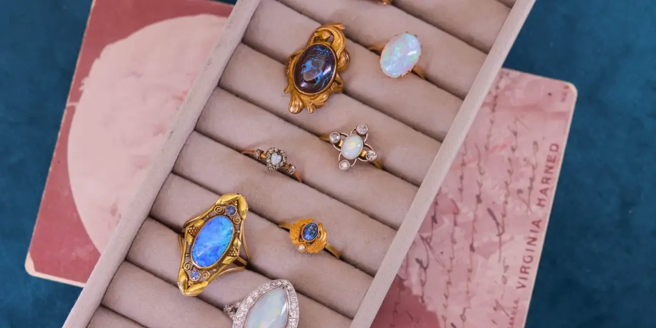 A collection of antique jewelry with opal stones, featuring rings with iridescent opals in gold settings, displayed in a velvet ring holder.