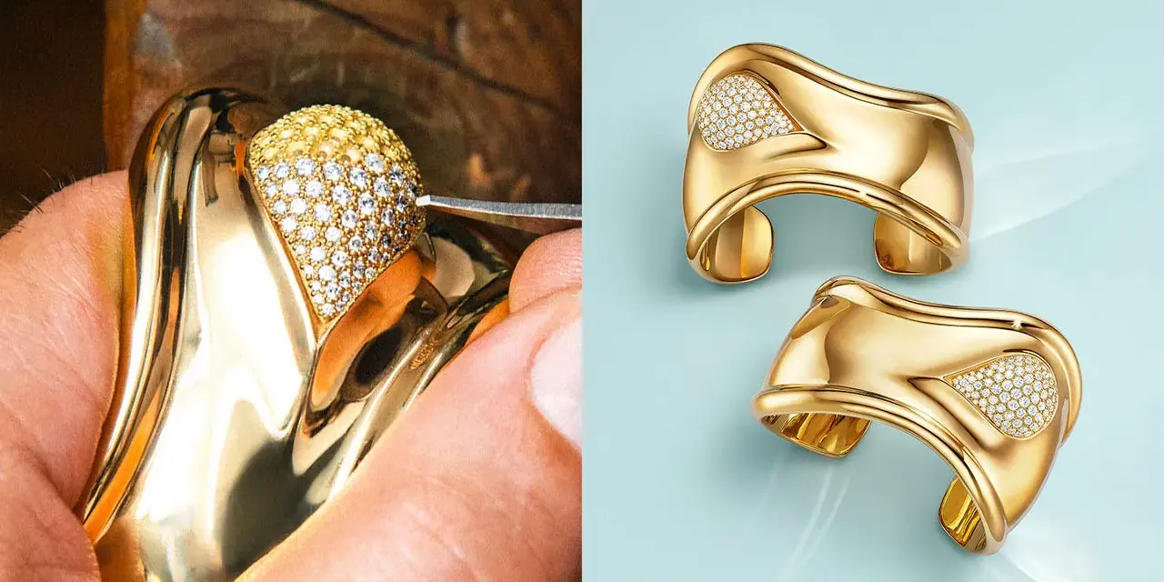 A jeweler meticulously sets diamonds on a gold ring, a testament to Elsa Peretti's exquisite designs. Two finished gold cuffs with diamond accents gleam on a light blue background.