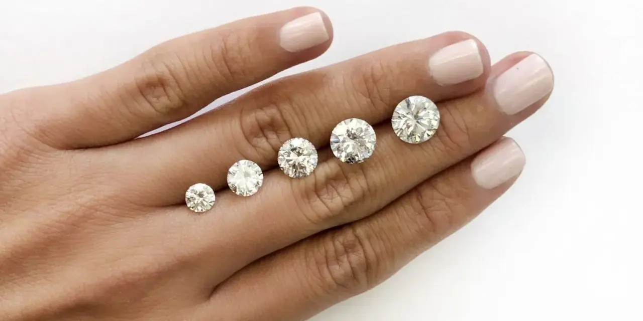 Five round brilliant cut diamonds are displayed on a hand, showing a progression in size. The largest diamond is what is considered a big diamond.