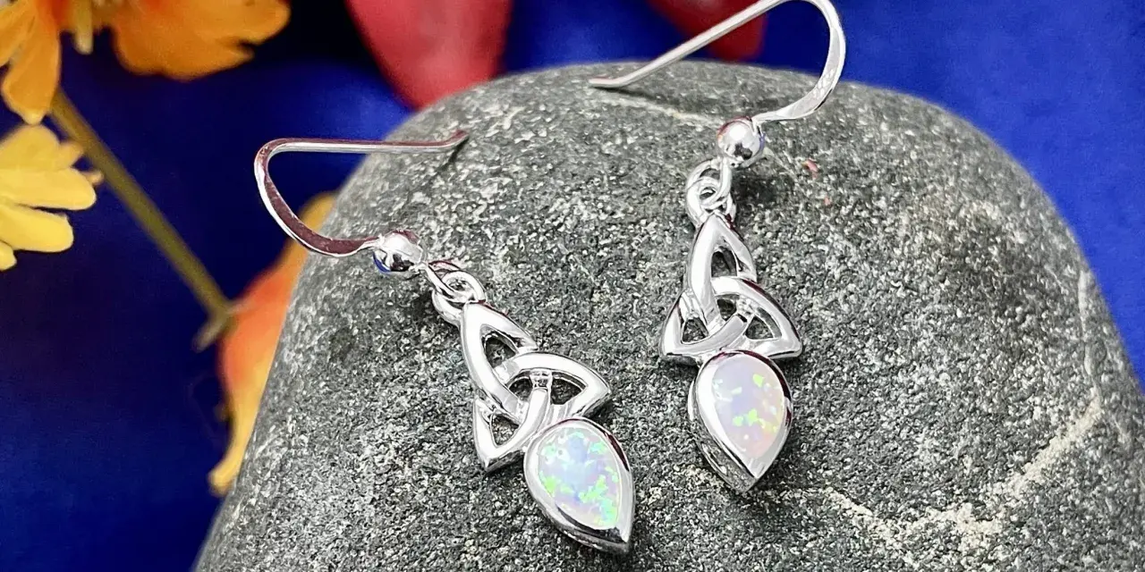 Silver Celtic knot earrings with opals, reminiscent of ancient Celtic birthstones, rest on a textured stone.