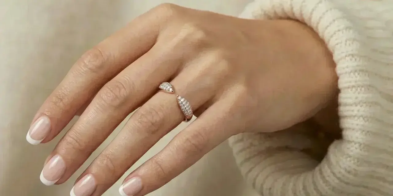 A hand with French manicured nails wears a sparkling rose gold ring. Rose gold is far from out of style!