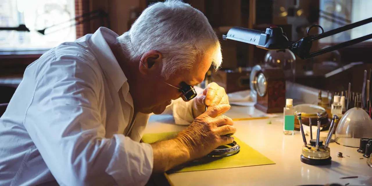 A watchmaker, wearing a loupe, meticulously works on a watch, demonstrating how to fix a watch with precision tools.