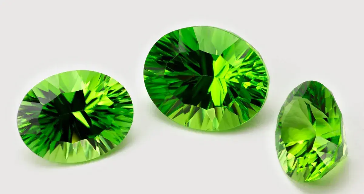 Three faceted peridots, the august 3rd birthstone, gleam with vibrant green light against a white background.