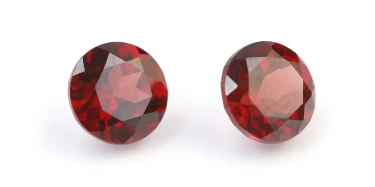Two deep red, faceted gemstones, the traditional capricorn birthstone, are displayed on a white background.
