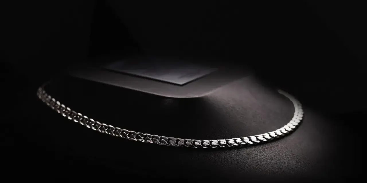 A sleek man platinum necklace rests on a dark, textured display.