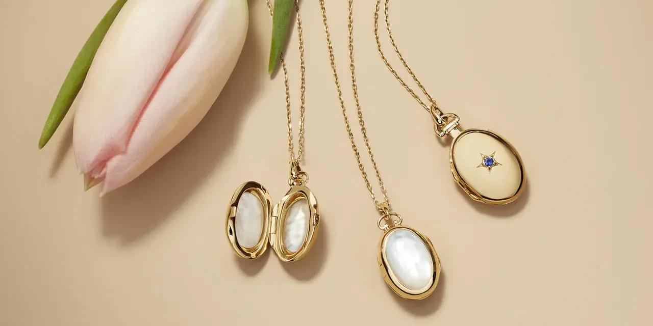 Gold lockets featuring mother of pearl, a lustrous material from shells, lie beside a delicate pink tulip.