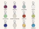 A collection of silver charms, each featuring a different colored gemstone representing birthstones for months: Garnet, Amethyst, Aquamarine, Crystal, Chrysoprase, Rainbow Moonstone, Carnelian, Peridot, Lapis, Opal, Citrine, and Turquoise.