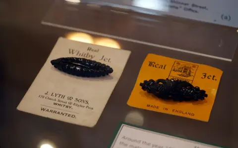 Two antique black jet stone brooches, one on a cream card from J. Lyth & Sons, Whitby, the other on a yellow card.