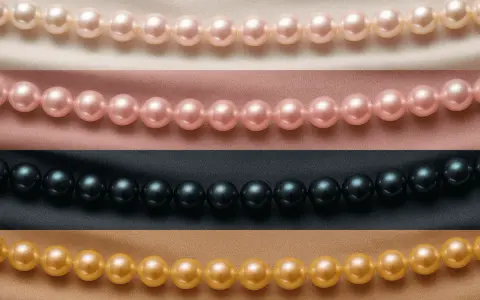 Rows of pearl color beads: cream, pink, black, and gold, draped on satin fabric.