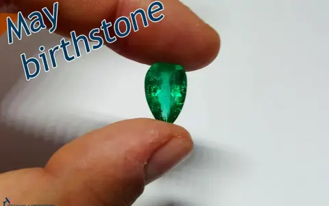 Fingers hold a pear-shaped emerald, the vibrant green gem representing the May birthstone.