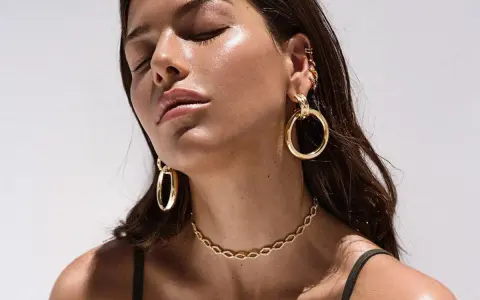 A woman with closed eyes showcases various types of dangling earrings, including large gold hoops and smaller ear cuffs.